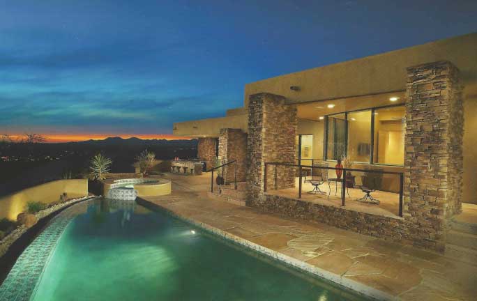 The backyard of a Tucson luxury home shot at sunset, featuring a beautiful hot tub and pool along with large glass windows