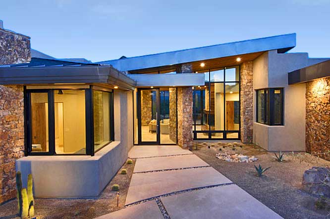 The contemporary entryway to a custom home with multiple large walls made of glass