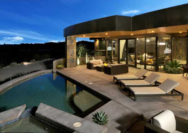 A contemporary luxury home with large glass windows and doors and a stone-lined swimming pool and spa
