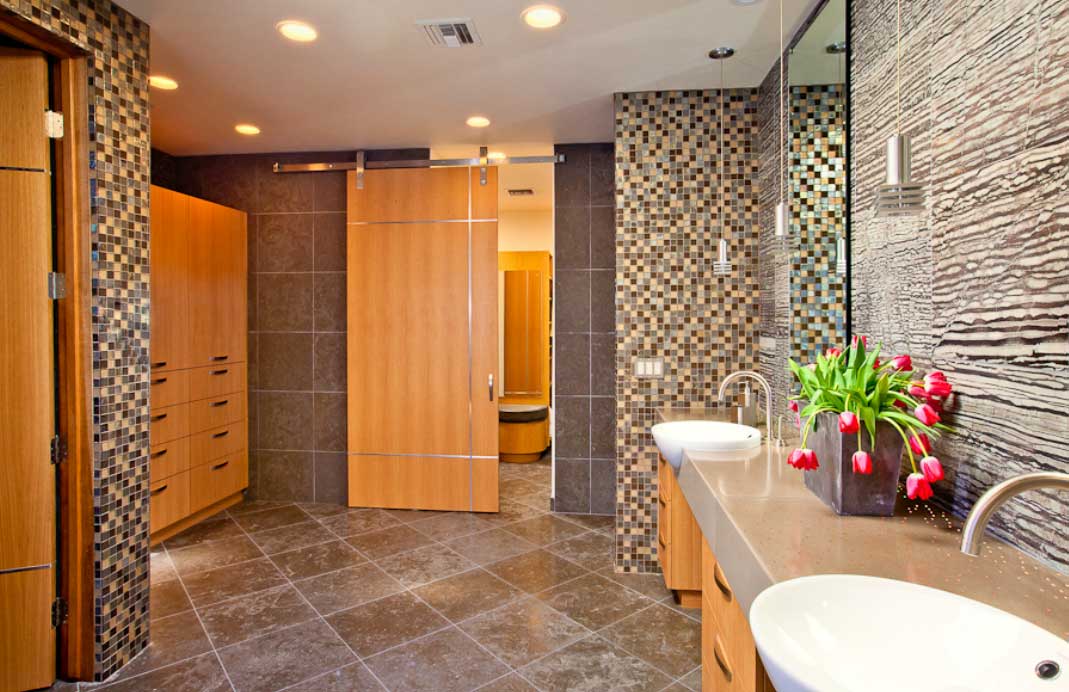 A bathroom in one of our luxury custom homes with stone tiles and wooden cabinets